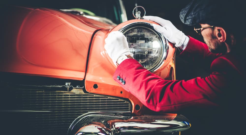 An older orange vehicle is shown having a headlamp installed by a mechanic.