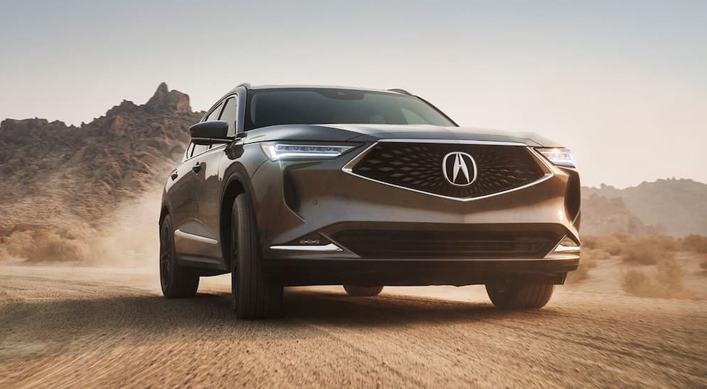 A bronze 2022 Acura MDX is shown on a dirt path after leaving a used car dealership.