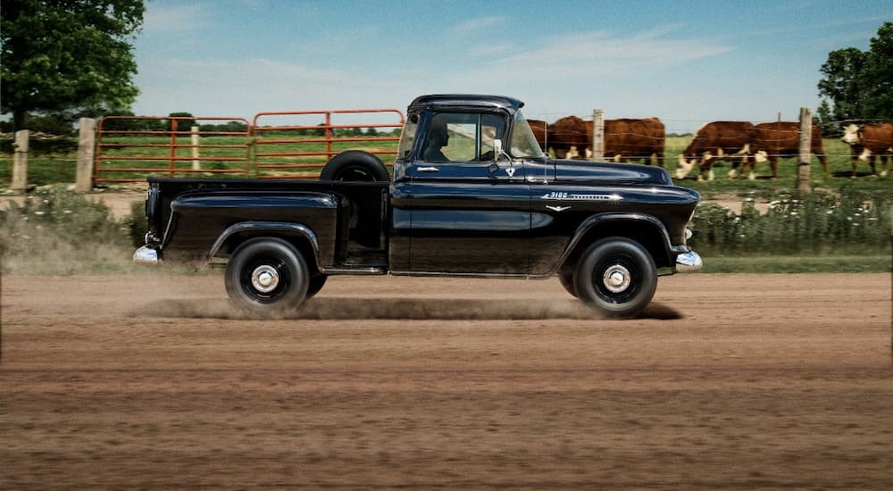 A rare used truck for sale, a black 1958 Chevy Task Force, is shown driving on a dirt road.