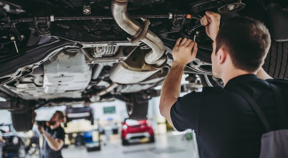 Two mechanics are seen working on the undercarriage of a vehicle.