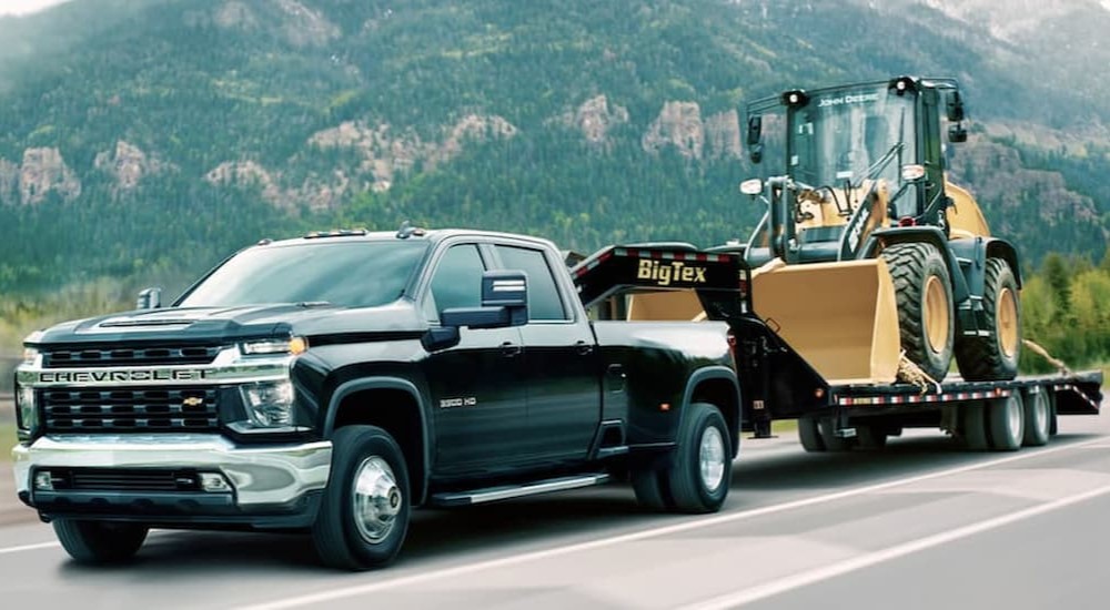 A black 2020 Chevy Silverado 3500 HD is shown towing heavy machinery.