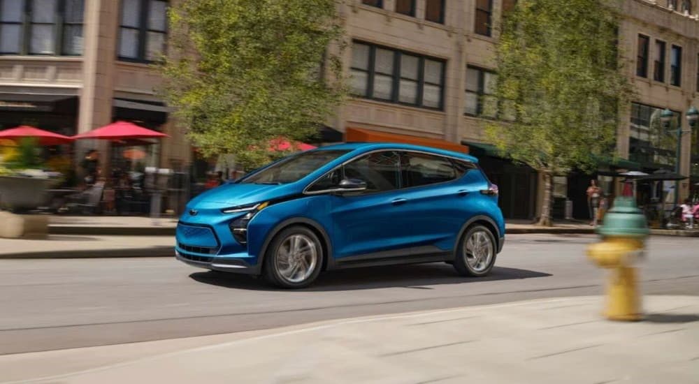 A blue 2023 Chevy Bolt EV is shown driving on a city street.