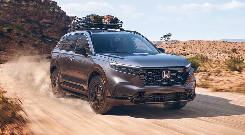 A gray 2023 Honda CR-V Hybrid Sport is shown driving on a dirt road.