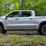 A silver 2023 Chevy Silverado for sale is show from the side parked in the woods.