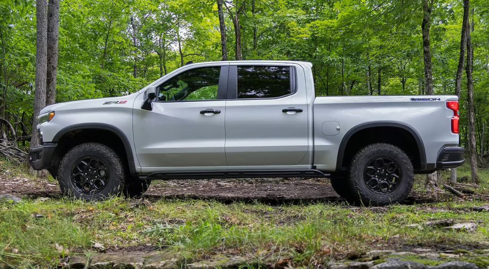 A silver 2023 Chevy Silverado for sale is show from the side parked in the woods.