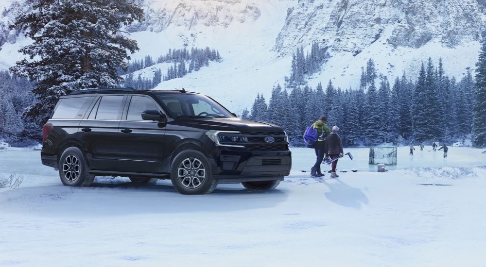 A black 2023 Ford Expedition is shown parked next to a frozen lake while a parent and child walk towards a hockey game to join.