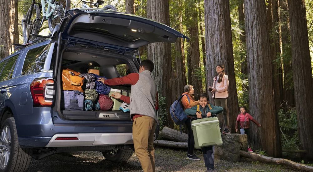 A family is shown packing bags into the cargo area of a blue 2023 Ford Expedition.