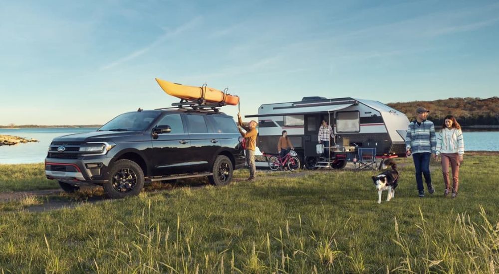 A family is shown camping with a set up white and gray trailer and black 2023 Ford Expedition Timberline by a lake. 