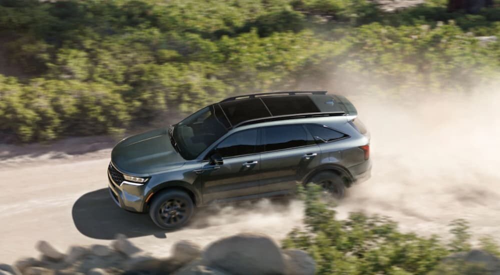 A green 2023 Kia Acadia is shown driving on a dirt road.