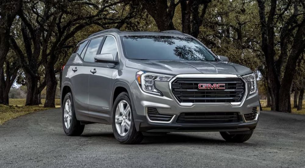 A gray 2023 GMC Terrain for sale is show parked in front of trees.