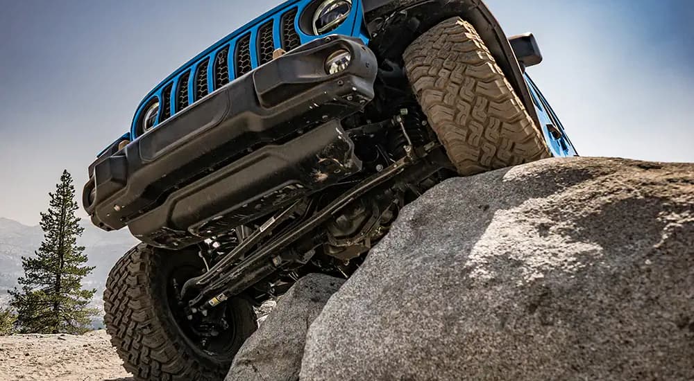 A blue 2023 Jeep Wrangler Rubicon 392 is shown demonstrating its articulation by climbing over a rock after getting a Jeep alignment.