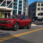 A red 2024 Chevy Trax is shown driving down a city street.