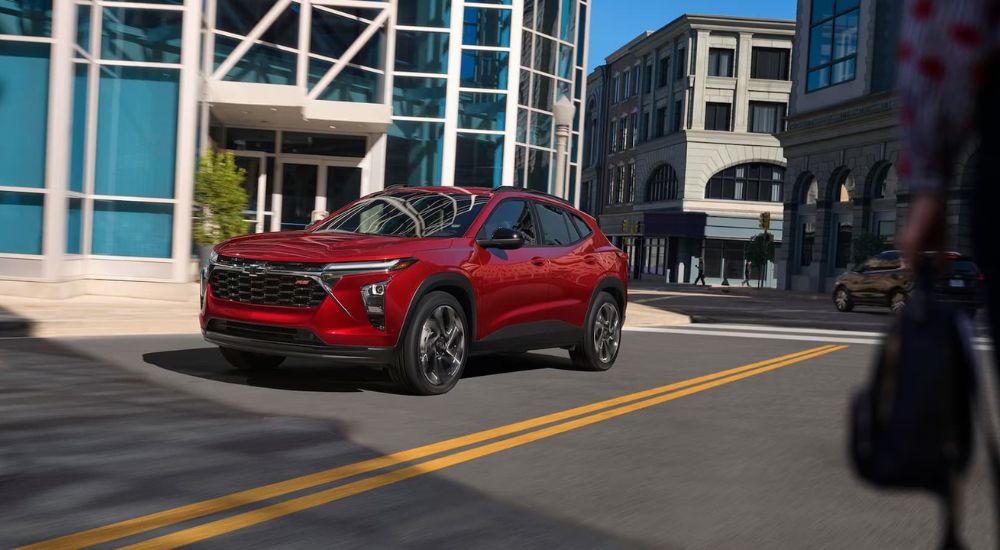 A red 2024 Chevy Trax is shown driving down a city street.
