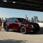 A red 2024 Mazda CX-90 for sale is parked in a parking garage with a woman walking next to it.