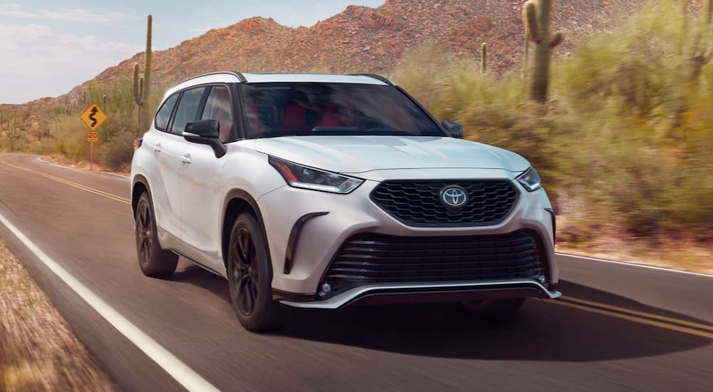 A white 2023 Toyota Highlander is shown driving on a highway.