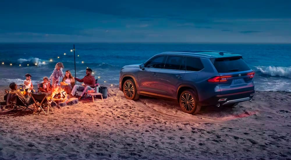 A blue 2024 Toyota Grand Highlander is shown parked on the sand near the ocean.