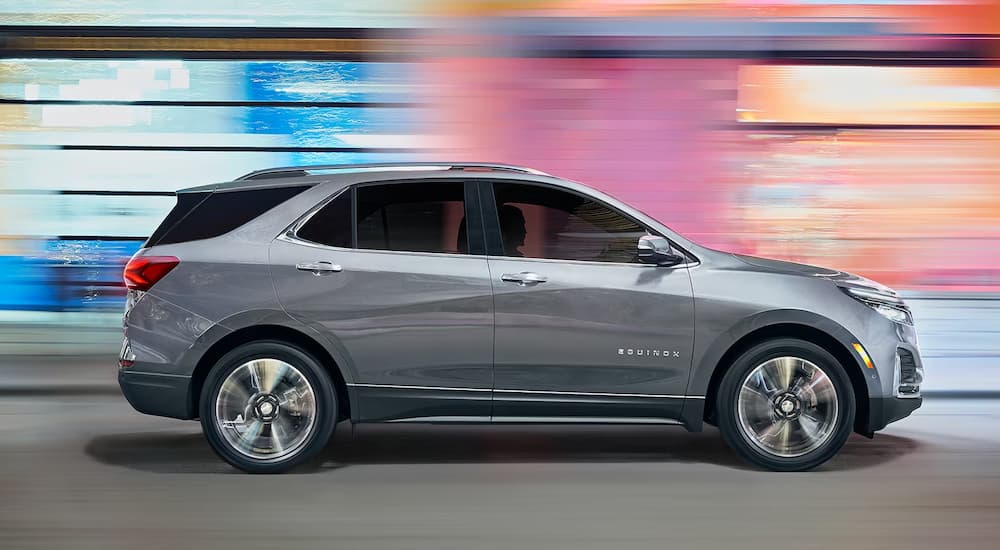 A gray 2023 Chevy Equinox for sale is shown drives past a blue and pink wall.