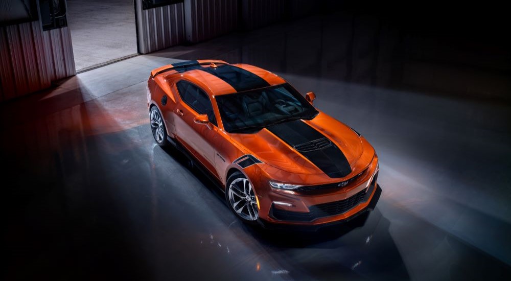 An orange and black 2023 Chevy Camaro is shown parked in a garage.