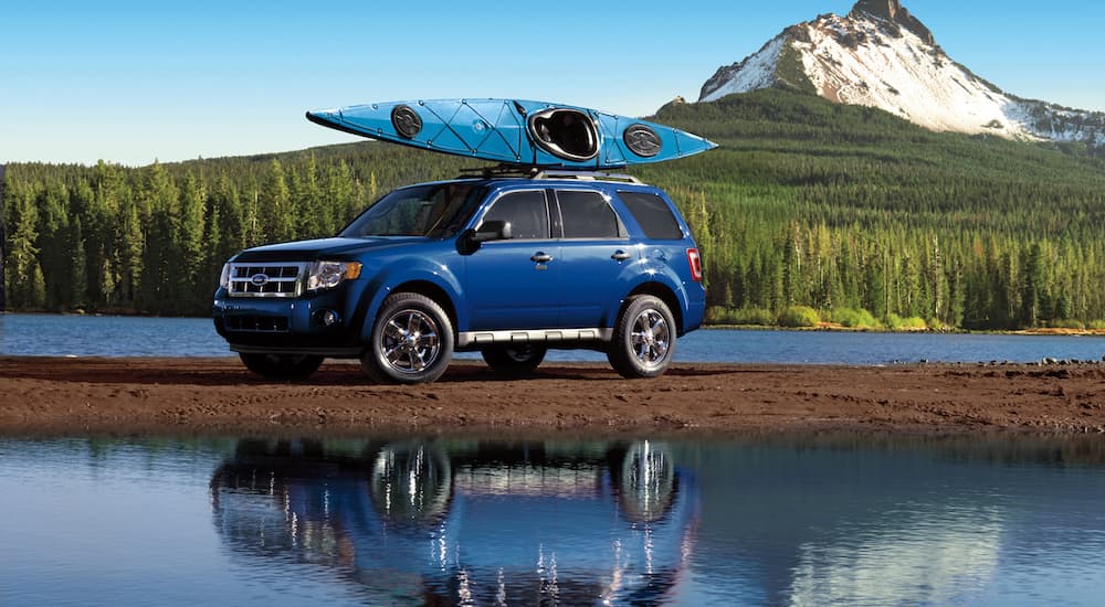 A blue 2010 Ford Escape is shown parked on the dirt in between two bodies of water.