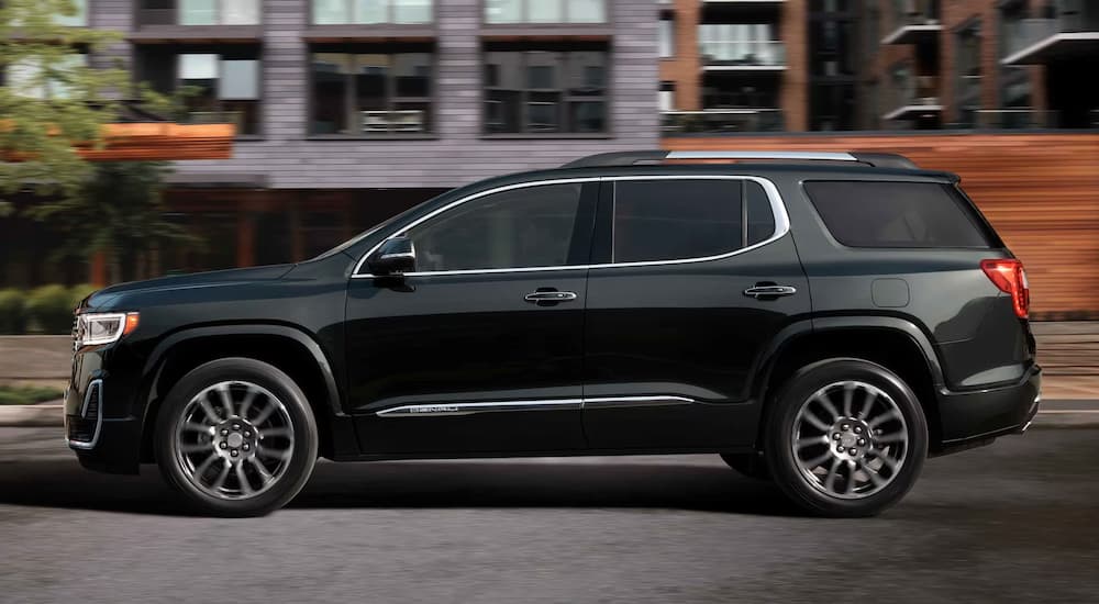 A black 2023 GMC Acadia Denali is shown driving down a city street away from a GMC dealer.