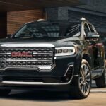 A man in a suit is shown opening the door of a black 2023 GMC Acadia Denali at a GMC dealer.