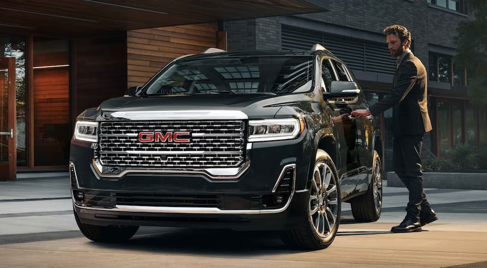 A man in a suit is shown opening the door of a black 2023 GMC Acadia Denali at a GMC dealer.