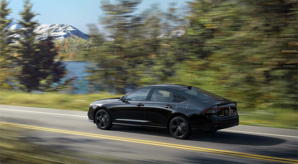 A black 2023 Honda Accord Sport-L Hybrid is shown cruising down a lakeside road.