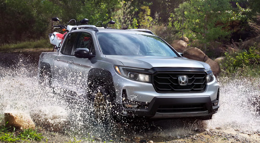A silver 2023 Honda Ridgeline is shown driving off-road.