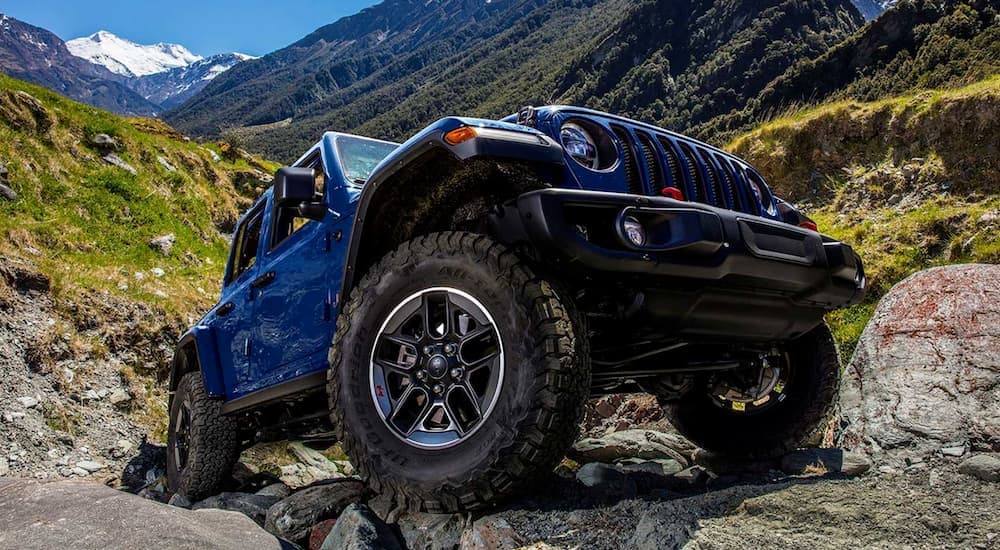A blue 2019 Jeep Wrangler Unlimited for sale is shown parked on rocks on a mountain.