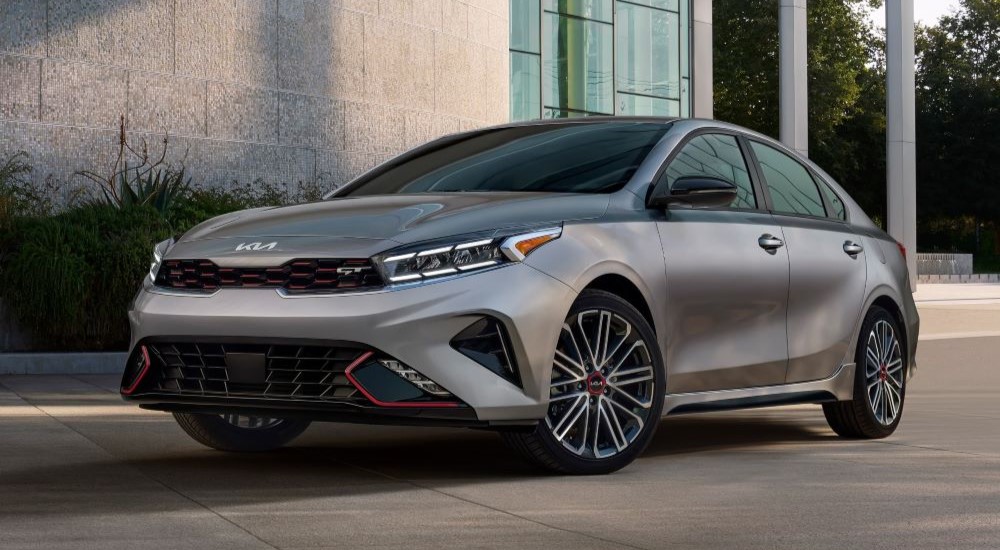 A silver 2023 Kia Forte GT is shown parked near a Kia dealership.