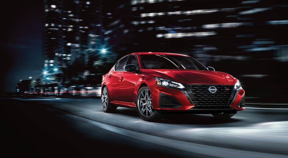 A red 2023 Nissan Altima SR is driving through a city at night.