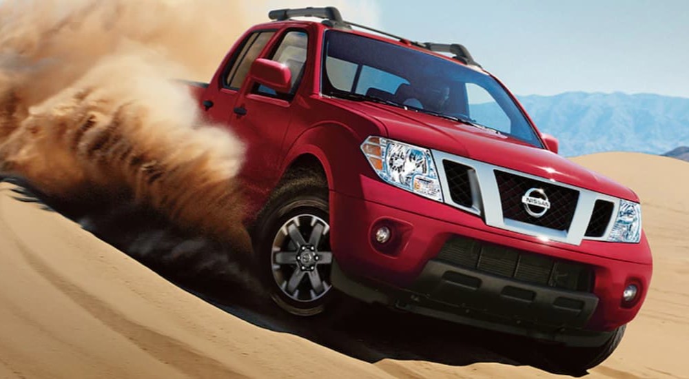 A red 2021 Nissan Frontier is shown driving on sand while off-roading.
