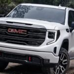 A white 2023 GMC Sierra 1500 is shown off-roading after visiting a used GMC Sierra dealer.