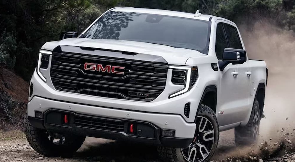 A white 2023 GMC Sierra 1500 is shown off-roading after visiting a used GMC Sierra dealer.