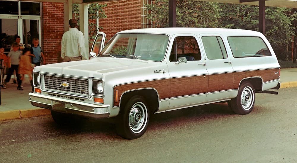 A white and brown 1973 Chevy Suburban is shown parked near a school after visiting a used GMC dealer.