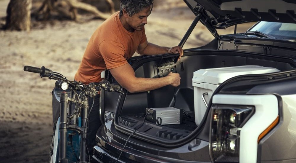 A man is shown plugging a device into an electrical outlet of a 2023 Ford F-150 Lightning.