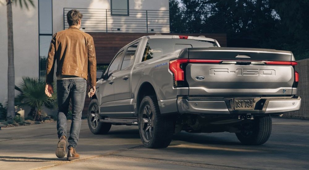 A silver 2023 Ford F-150 Lightning is shown parked on a driveway near a person walking.