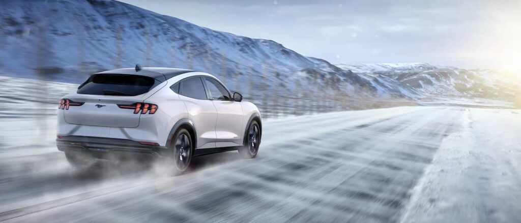 A white 2023 Ford Mustang Mach-E is shown driving near a mountain.