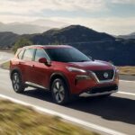 A red 2023 Nissan Rogue is shown driving on a highway.