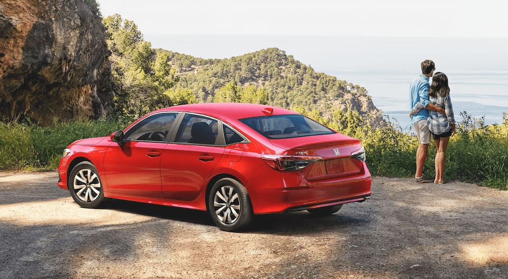 A red 2023 Honda Civic LX is shown parked by a mountain hiking trail.