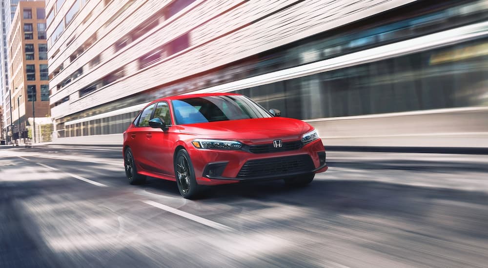 A red 2023 Honda Civic Touring is shown driving on a city street.