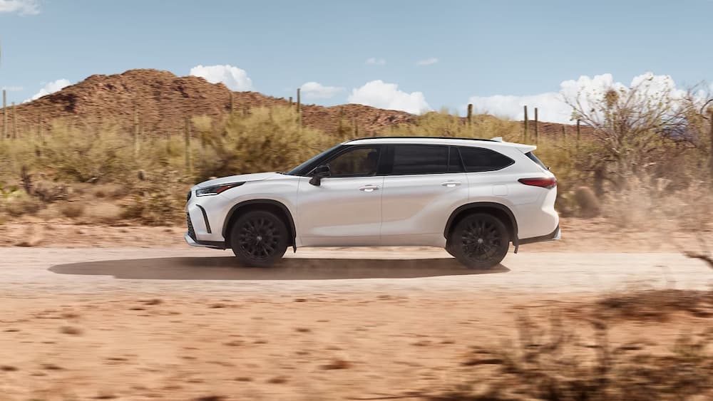 A white 2023 Toyota Highlander is shown driving on a dirt road.
