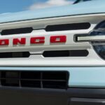 The Oxford white grille with red Bronco lettering is shown on a light blue 2023 Ford Bronco Heritage Edition.