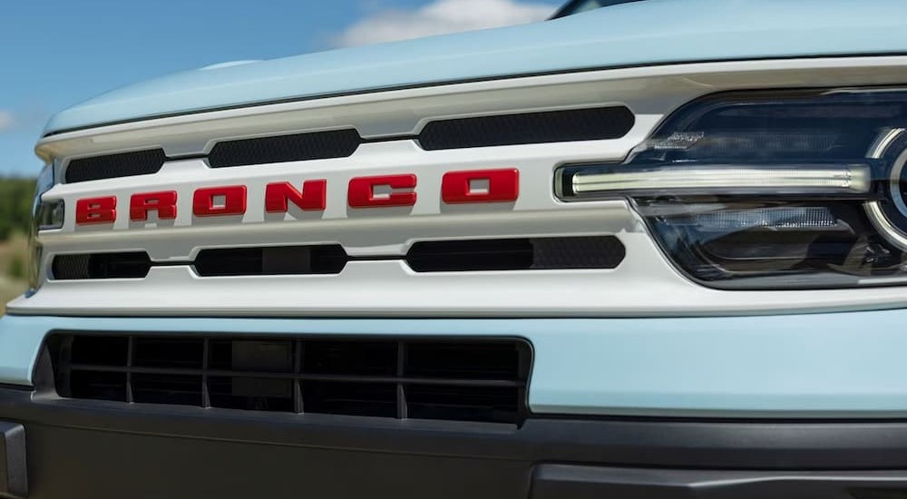 The Oxford white grille with red Bronco lettering is shown on a light blue 2023 Ford Bronco Heritage Edition.