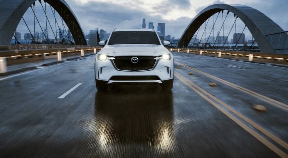 A white 2024 Mazda CX-90 PHEV is shown driving on a bridge.