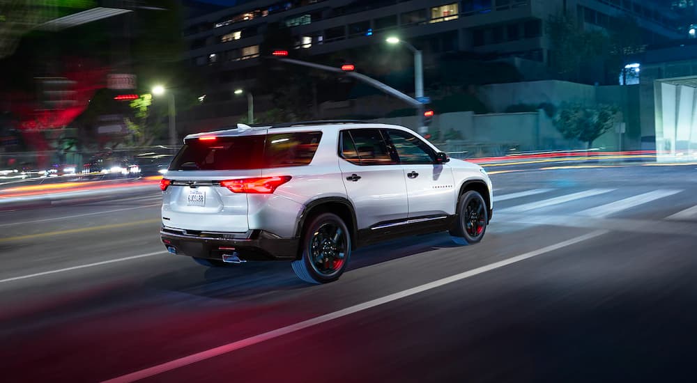 A white 2023 Chevy Traverse Redline is shown driving on a city street at night.