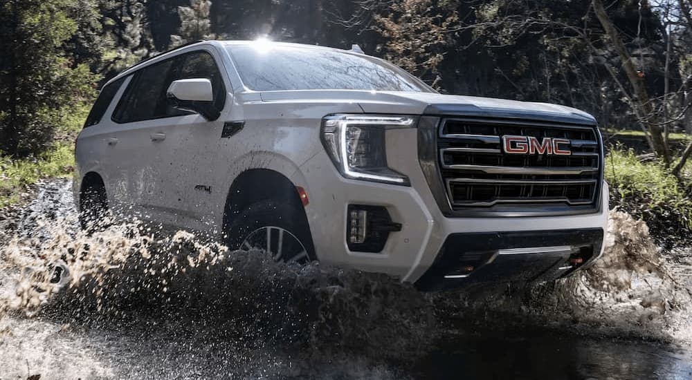 A white 2023 GMC Yukon AT4 is shown driving off-road through water.