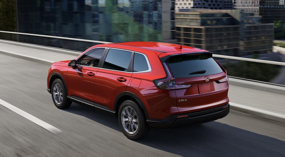 A popular Honda CR-V for sale, a red 2023 Honda CR-V, is shown driving near a city.