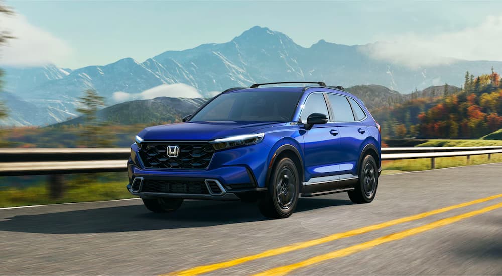 A blue 2023 Honda CR-V Hybrid Sport Touring is shown driving on a highway.