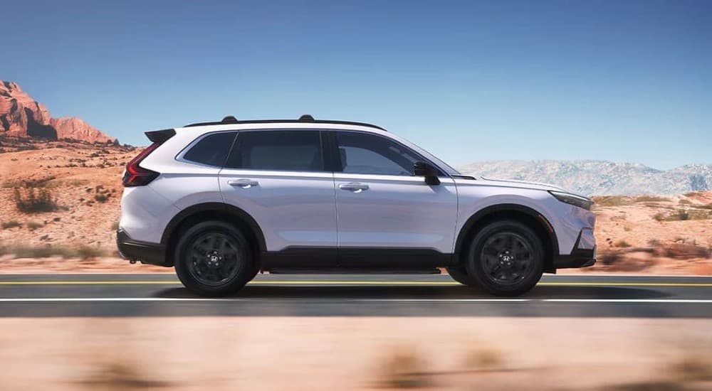 A white 2023 Honda CR-V Sport Touring Hybrid is shown driving on a highway after viewing cars for sale.